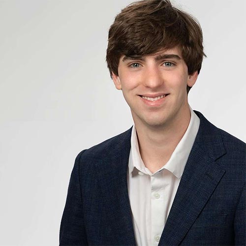 Professional headshot of a smiling young man in a dark suit jacket and white shirt.