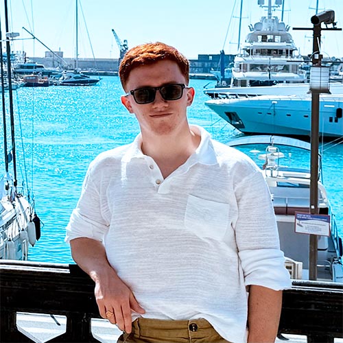 Young man in sunglasses and white shirt by a sunny marina with boats and yachts.